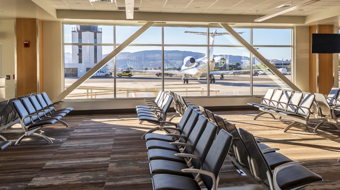 In the SLO Airport, at terminal gate area. Can see four rows of chairs against large window where a small airplane is parked and the airport tower can also be seen.