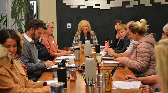 People are seated around the SLO Chamber conference table, smiling at each other and in a discussion. They have papers and coffee mugs in front of them.