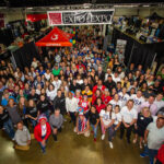 Large group aerial photo with everyone looking up towards camera in a large hall. Above their heads there is a banner that reads, San Luis Obispo Chamber of Commerce, EXPO at the Expo