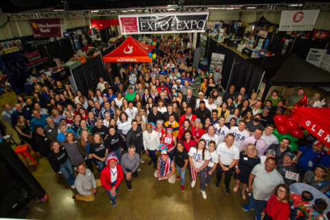 Large group aerial photo with everyone looking up towards camera in a large hall. Above their heads there is a banner that reads, San Luis Obispo Chamber of Commerce, EXPO at the Expo