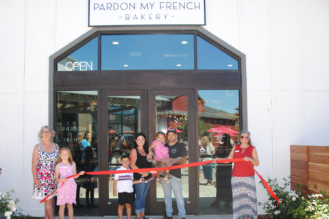 Group shot of people posing for a ribbon cutting in front of the storefront, Pardon My French Bakery.