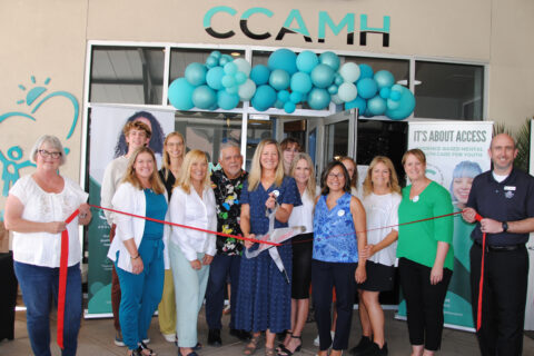 A group of people in front of CCAMH during a ribbon cutting celeebration. A bunch of blue and white balloons in the background.