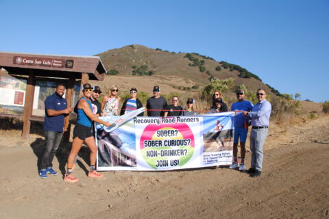 Group of people standing inform of Cerro Trail with mountain in the background celebrating a ribbon cutting