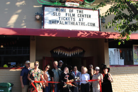 Group of people in front of the Palm Theatre in SLO celebrating with a ribbon cutting