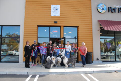 Large group of people with some dogs posing for a ribbon cutting photo.