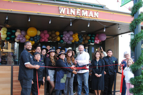 Group of people in front of a restuarant posing for a ribbon cutting photo.