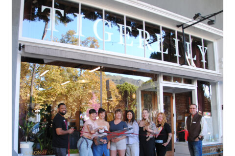 Group picture standing in front of the storefront, Tigerlily Salon in Downtown SLO, smiling for a ribbon cutting photo.