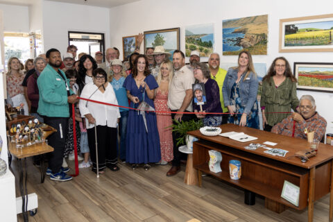 Group shot of people inside and art studio taking a ribbon cutting photo